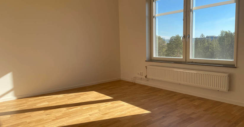 Sol skiner in genom fönster på golv i tom lägenhet