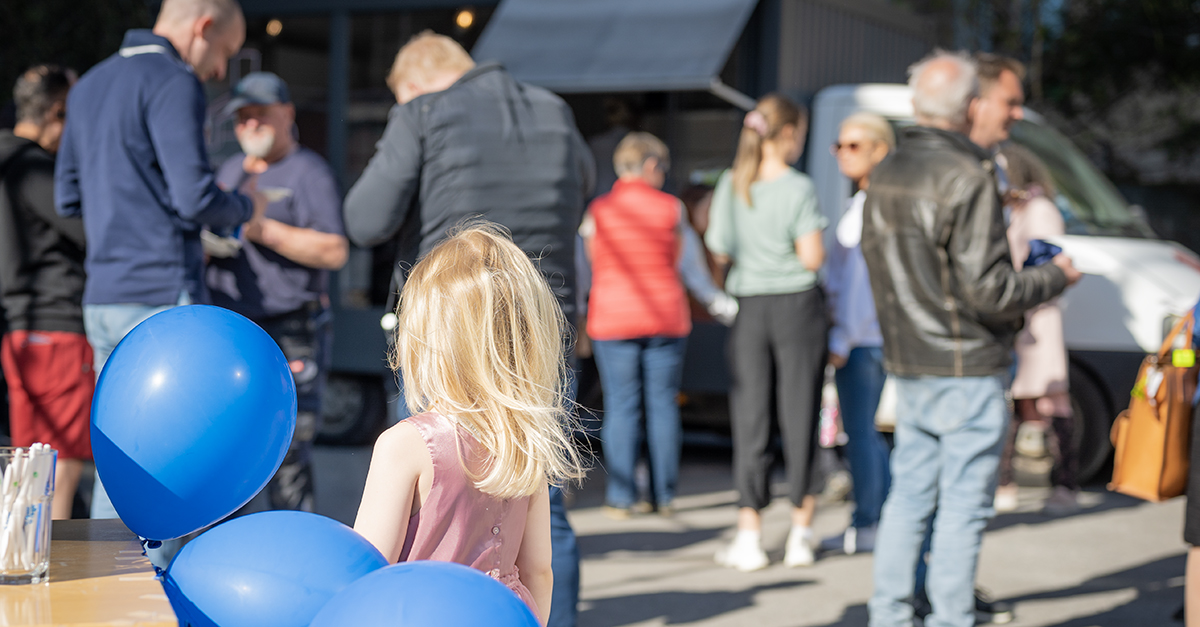 Ballonger och ett barn i förgrunden framför människor som mingar och äter pizza.