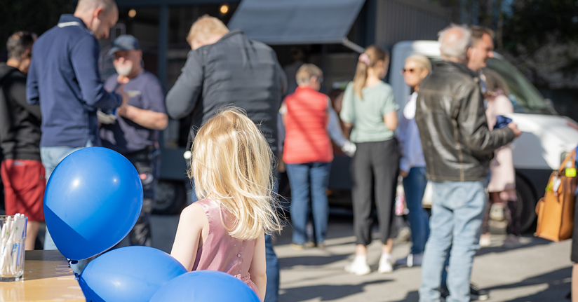 Ballonger och ett barn i förgrunden framför människor som mingar och äter pizza.